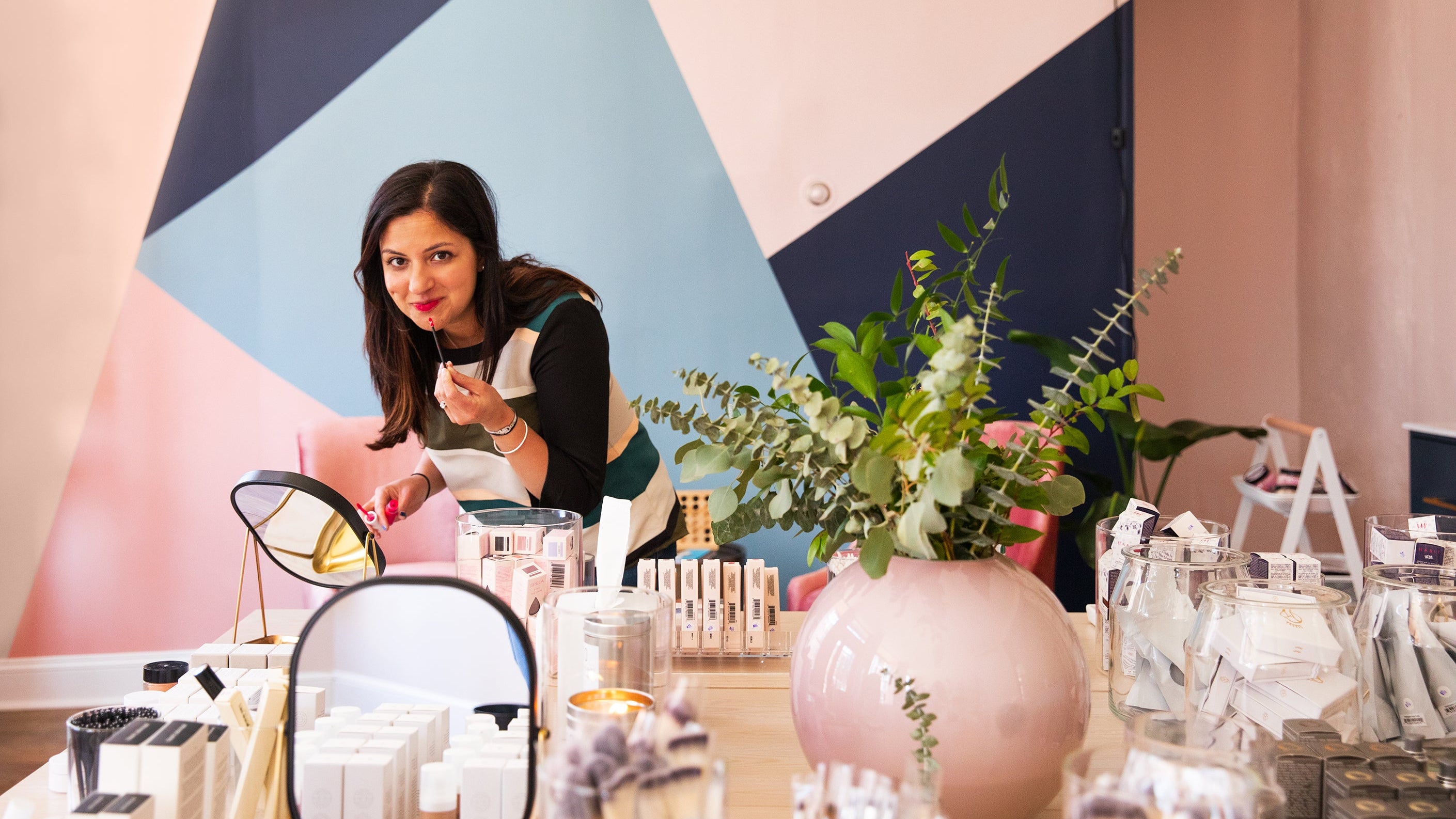 Woman standing behind a counter with decorative items and plants in a stylish interior.